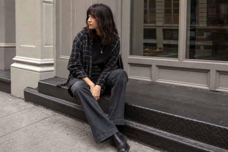 Grunge capsule wardrobe essentials laid out with plaid flannel, dark denim, black tee, chunky boots and knit layers