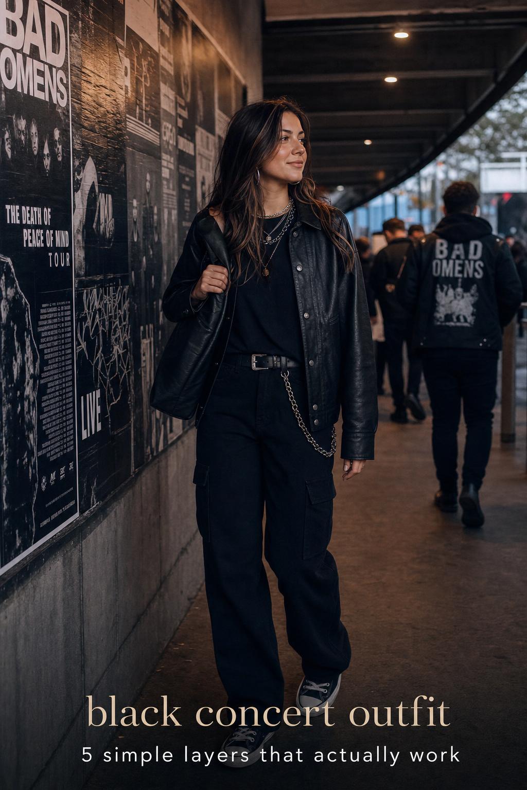 Black concert outfit with layered jacket, cargo pants, and boots outside a venue at dusk, urban pre-show atmosphere
