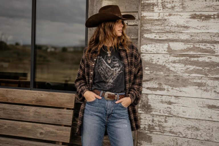Grunge cowgirl outfits with faded plaid shirt, straight-leg denim, and dark leather cowboy boots in a natural outdoor setting