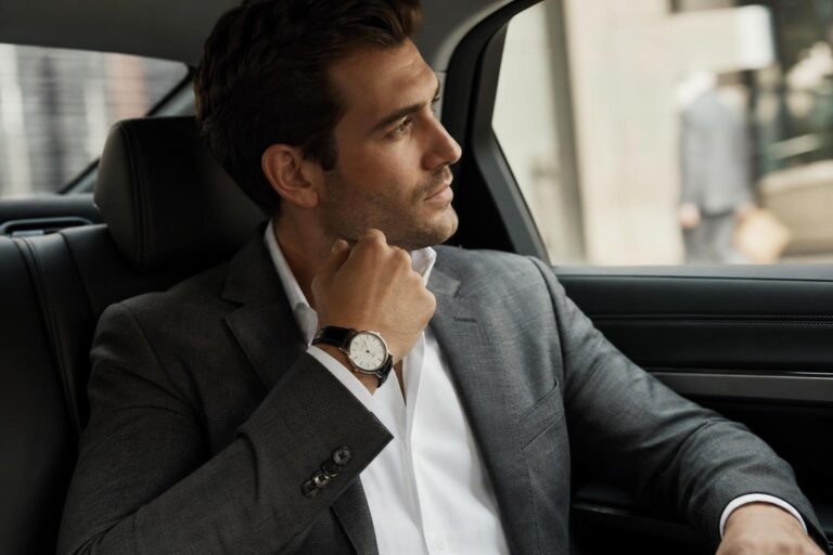 Old money watches on a leather strap peeking from a tailored suit cuff, showing a slim case and clean dial.
